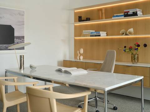 Geiger One Casegoods in Nordic Oak veneer shown at an angle with freestanding Parsons table with white marble top, Taper chair, and two Lijn Armchairs for guests in a private office setting